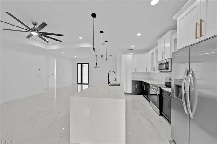 Kitchen with white cabinetry, decorative light fixtures, stainless steel appliances, light stone countertops, and ceiling fan