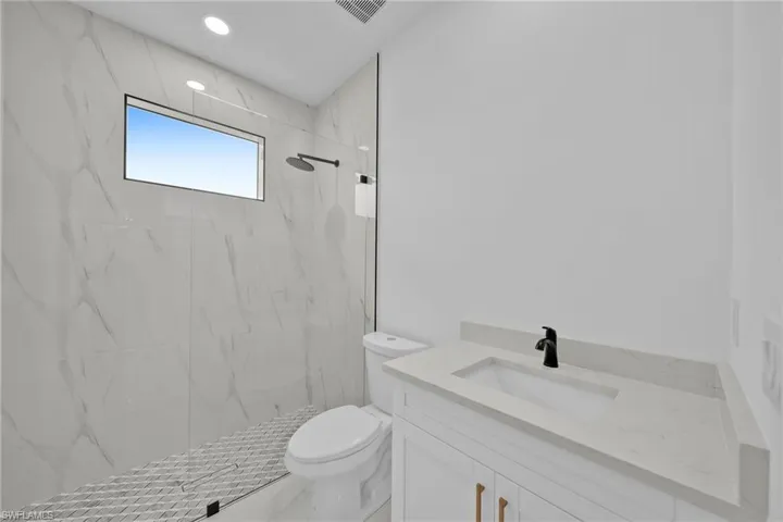 Bathroom featuring tiled shower, vanity, and toilet