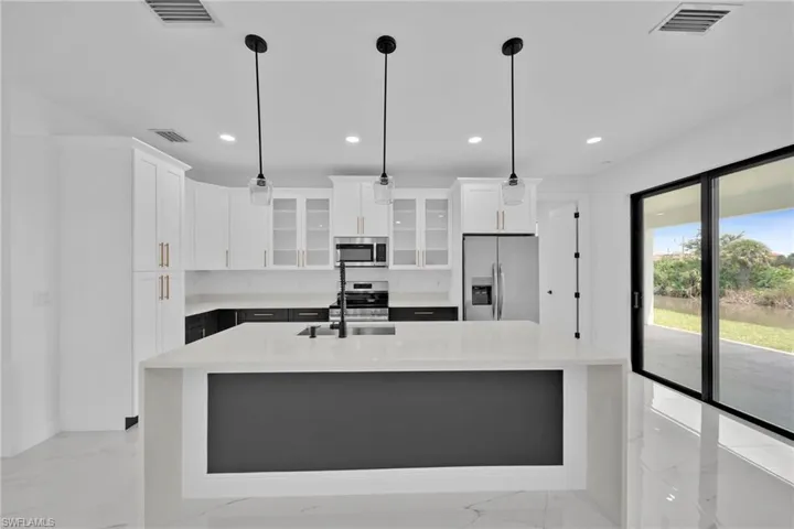 Kitchen with a center island with sink, pendant lighting, appliances with stainless steel finishes, and white cabinetry