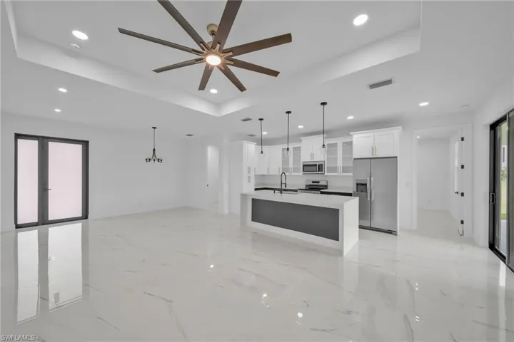 Kitchen featuring a kitchen island with sink, white cabinetry, decorative light fixtures, stainless steel appliances, and ceiling fan