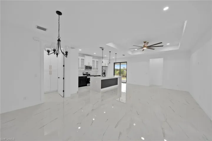 Unfurnished living room featuring ceiling fan with notable chandelier, a raised ceiling, and sink