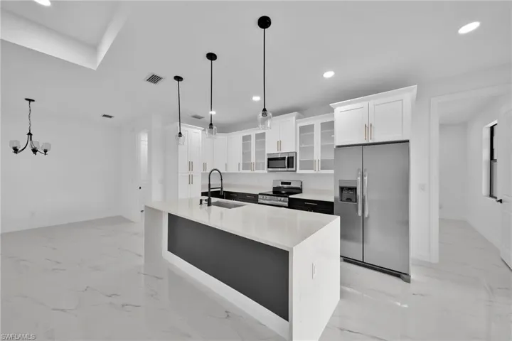 Kitchen featuring a center island with sink, hanging light fixtures, stainless steel appliances, sink, and white cabinets