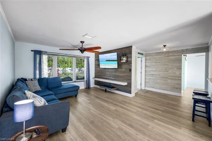 Living room with light wood-type flooring, baseboards, ornamental molding, and a ceiling fan