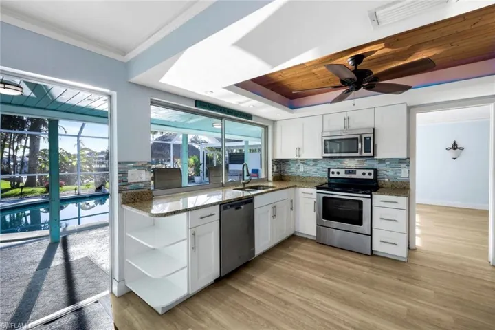Kitchen with open shelves, a sink, appliances with stainless steel finishes, white cabinetry, and a raised ceiling
