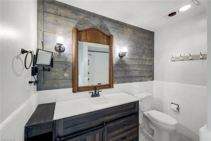 Bathroom with toilet, tile walls, wainscoting, and vanity