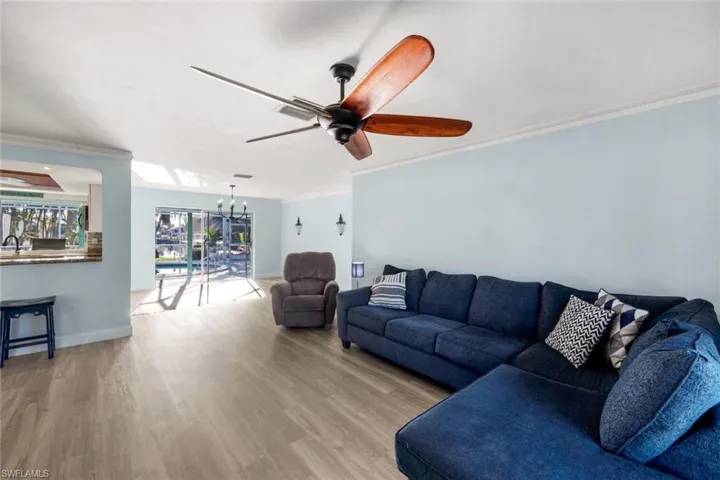 Living area featuring wood finished floors, baseboards, visible vents, crown molding, and ceiling fan with notable chandelier
