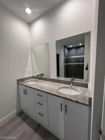 Bathroom featuring double vanity, light wood finished floors, tiled shower, and recessed lighting