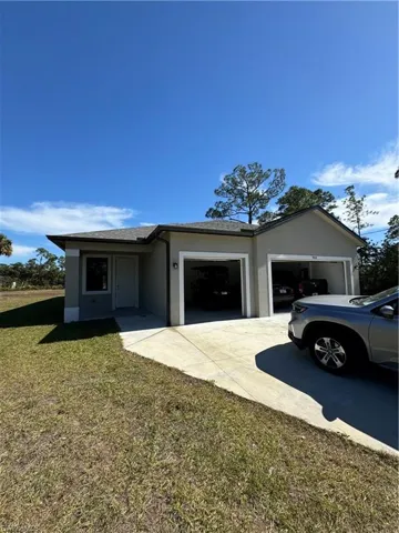 View of front facade featuring stucco siding, a garage, a front lawn, driveway, and roof with shingles