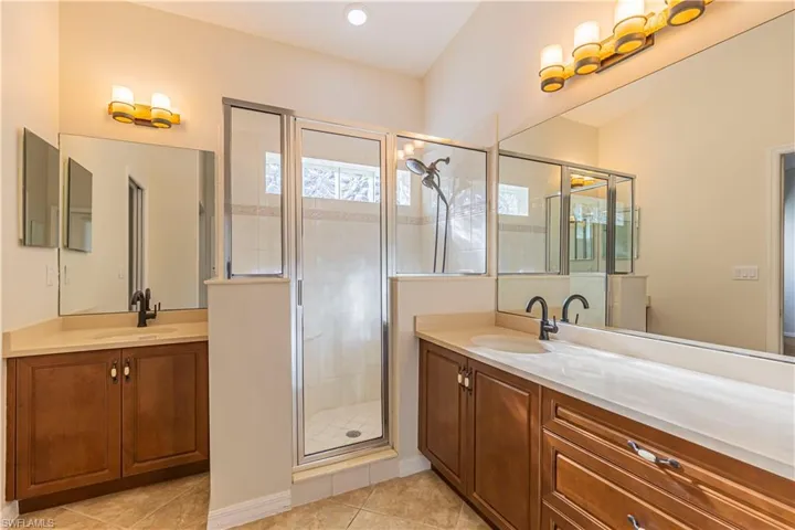 Bathroom featuring two vanities, a sink, a stall shower, and tile patterned flooring