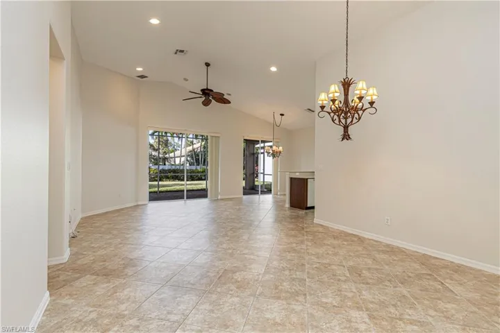 Unfurnished living room with ceiling fan with notable chandelier, visible vents, and baseboards