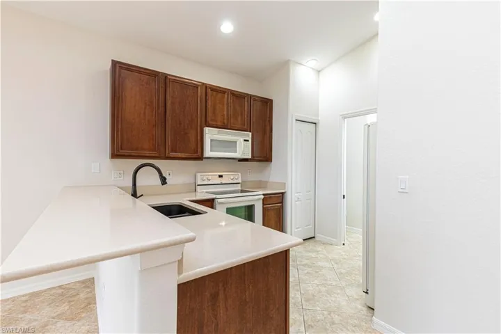 Kitchen with light countertops, white appliances, light tile patterned floors, a sink, and a peninsula