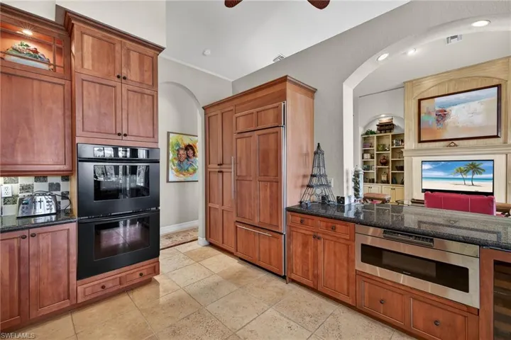 Kitchen with brown cabinets, paneled built in fridge, dark stone countertops, and beverage cooler