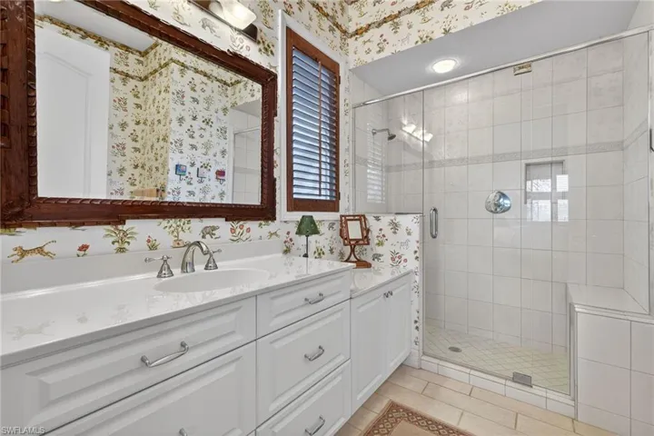 Bathroom with wallpapered walls, vanity, a shower stall, and light tile patterned flooring
