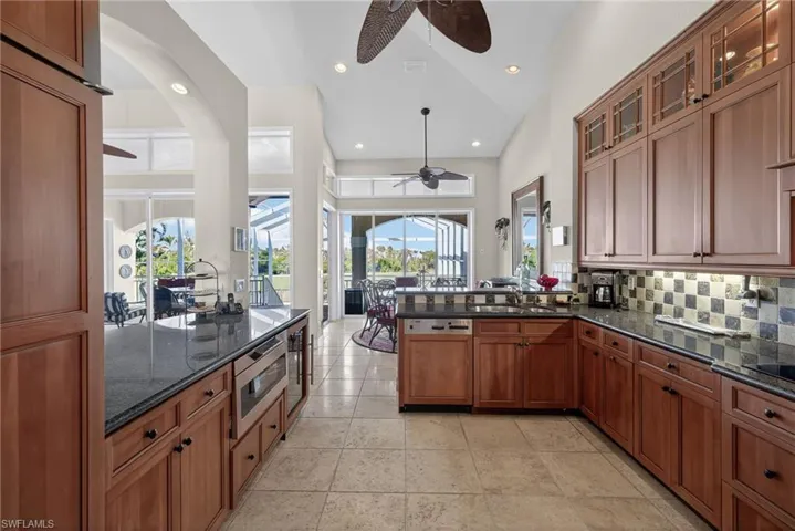 Kitchen with brown cabinets, a peninsula, backsplash, dark stone counters, and recessed lighting