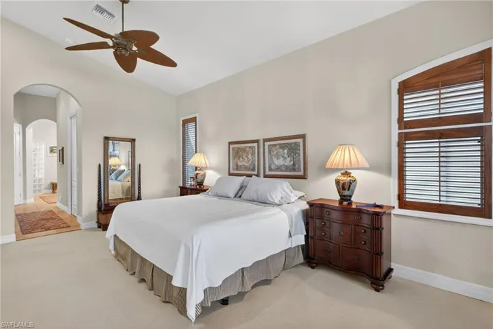 Primary Bedroom featuring arched walkways, vaulted ceiling, a ceiling fan, light colored carpet, and ensuite bathroom