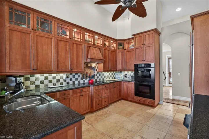 Kitchen featuring glass insert cabinets, brown cabinetry, black appliances, arched walkways, and ceiling fan