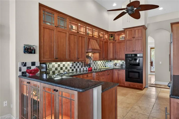 Kitchen with brown cabinetry, arched walkways, tasteful backsplash, dark stone countertops, and recessed lighting