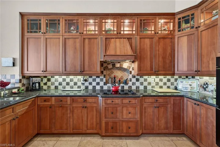 Kitchen with dark stone countertops, brown cabinetry, glass insert cabinets, and custom exhaust hood