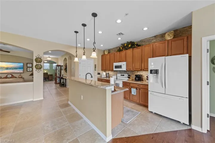 Kitchen with hanging light fixtures, white appliances, light stone countertops, sink, and an island with sink