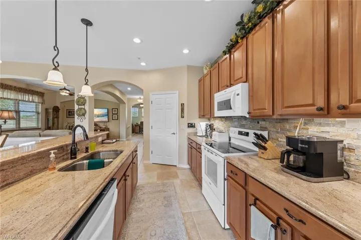 Kitchen with light tile patterned floors, decorative light fixtures, white appliances, light stone countertops, and sink