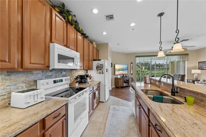 Kitchen with white appliances, light stone counters, sink, hanging light fixtures, and light hardwood / wood-style floors