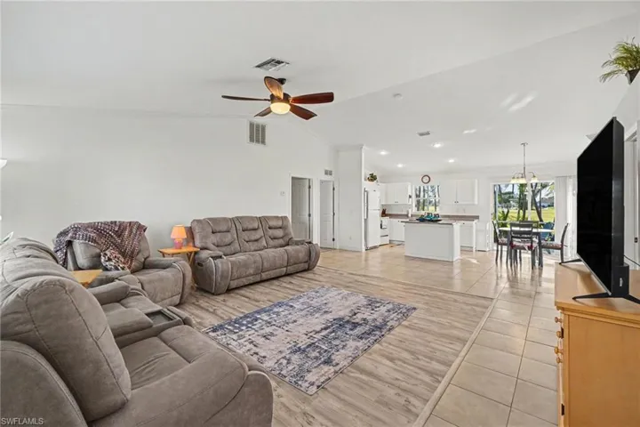Open-concept interior featuring vaulted ceilings, wood-finish laminate and tile flooring , recessed lighting, a ceiling fan with integrated light fixture, and a kitchen island