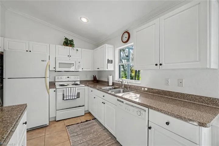 Kitchen featuring white shaker-style cabinetry, solid-surface countertops, dual-basin stainless steel sink, and recessed lighting