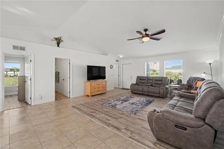 Open-concept living space featuring vaulted ceilings, neutral wall tones, large-format tile flooring, wood-finish flooring insets sourrounded by tile, and a central ceiling fan