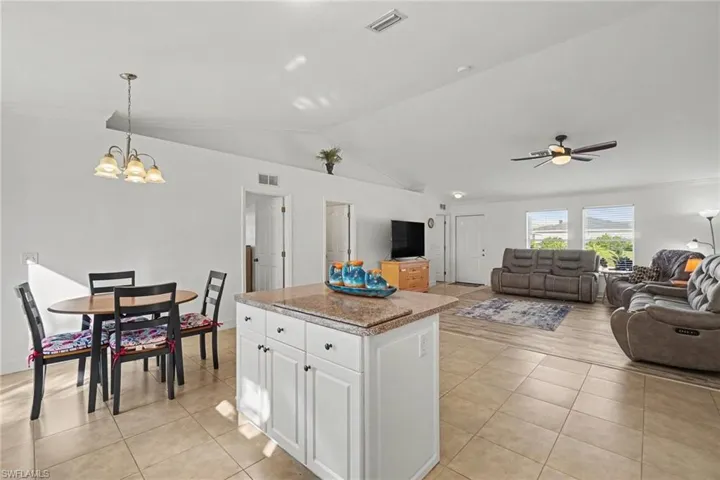 Open-concept interior featuring vaulted ceilings, a central kitchen island with a stone-finish countertop, ceramic tile flooring, a multi-arm chandelier, and a ceiling fan