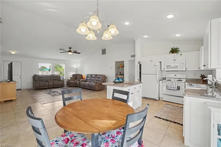 Open-concept living space featuring ceramic tile flooring, vaulted ceilings, a central kitchen island with stone-finish countertops, crisp white cabinetry, and a multi-arm chandelier