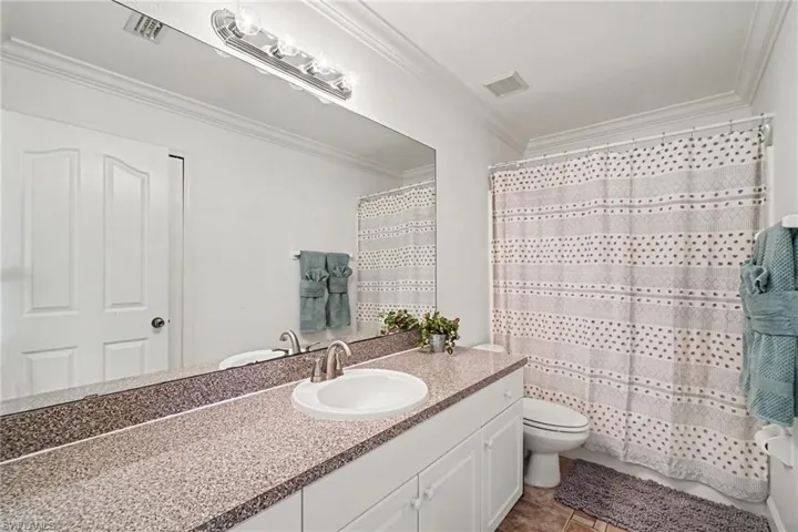 Bathroom featuring an extended vanity with a neutral-tone countertop, an integrated round sink, a full-width wall mirror, and a classic four-bulb overhead vanity light