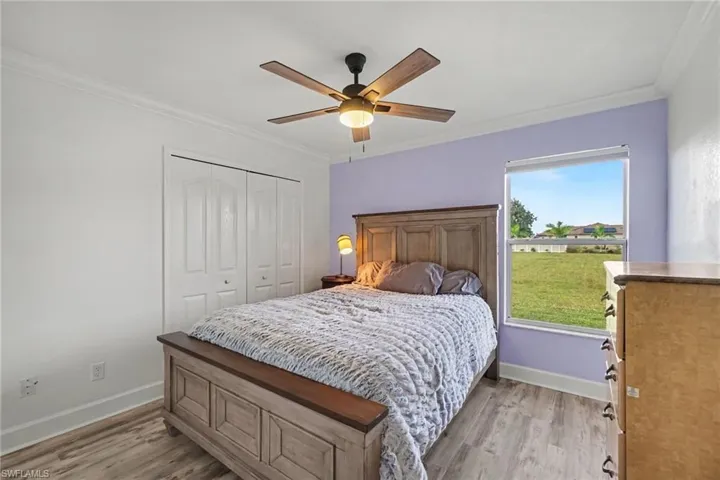 Room featuring wood-finish flooring, a multi-blade ceiling fan with integrated lighting, dual-panel sliding closet doors, and a single-pane window with exterior greenery