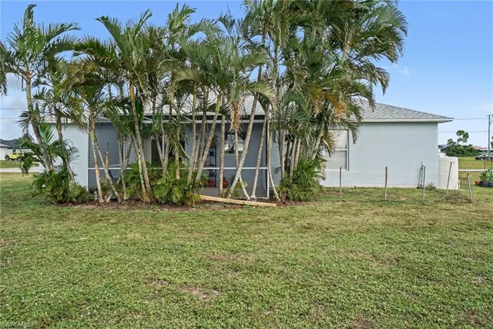 Exterior featuring a screened-in lanai, mature palm trees, shingle roofing, and expansive lawn space