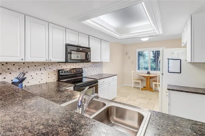 Kitchen featuring backsplash, a tray ceiling, white cabinetry, black appliances, and light tile floors