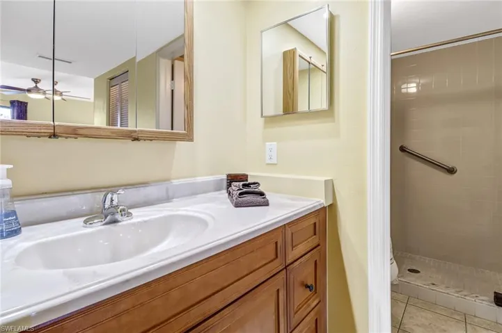Bathroom with tile floors, ceiling fan, tiled shower, and large vanity