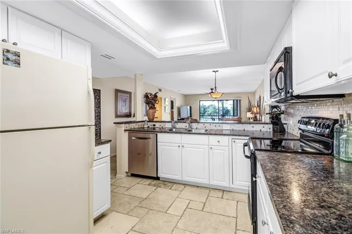 Kitchen with kitchen peninsula, stainless steel dishwasher, white fridge, black electric range, and white cabinetry
