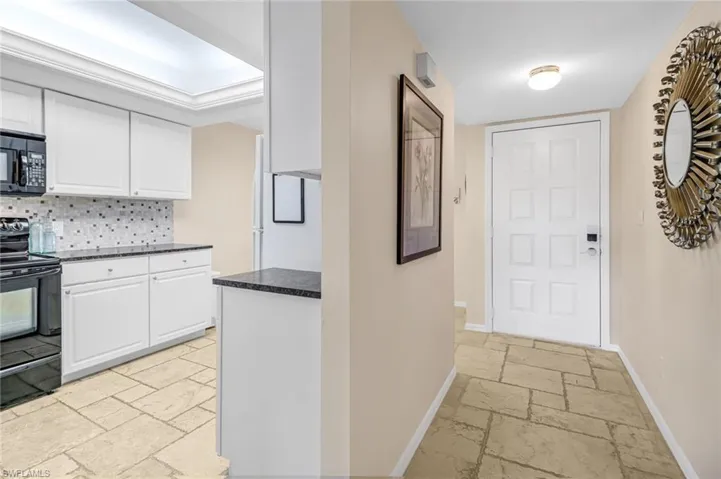 Kitchen with white cabinetry, light tile flooring, backsplash, and black appliances