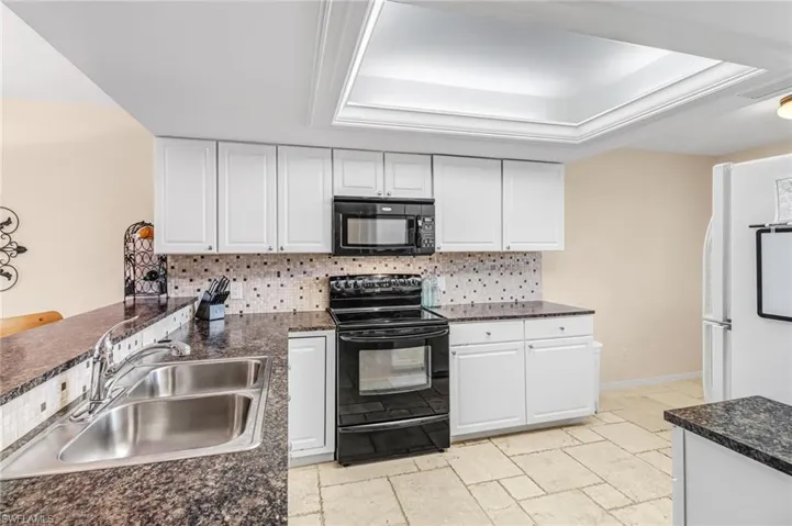 Kitchen featuring a tray ceiling, black appliances, white cabinets, and backsplash