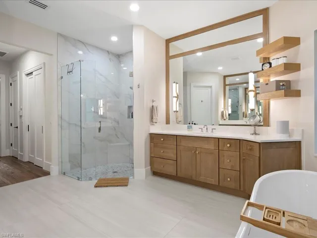 Standout features of the bathroom remodel are the oversized vanities with quartz countertops and floating shelves accented by newly installed pendant lights. The natural stone shower is oversized and boasts multiple shower heads.