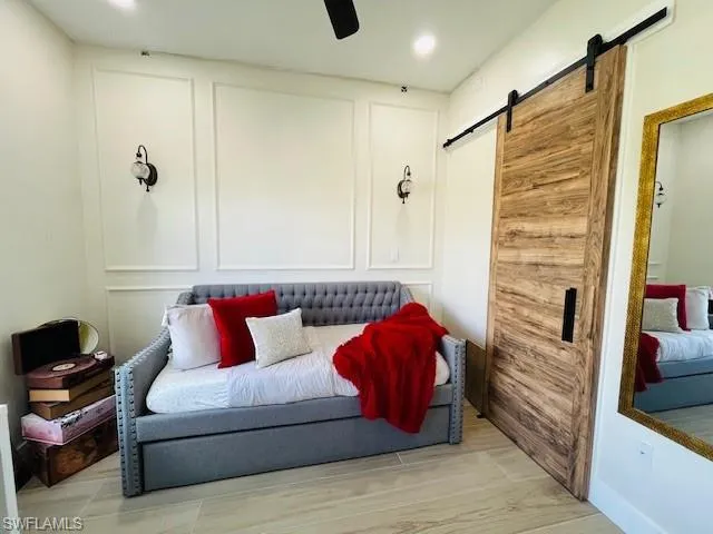 Living area featuring a decorative wall, a barn door, ceiling fan, and wood finished floors