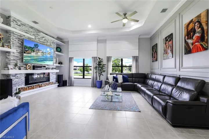 Living room with built in features, a fireplace, a ceiling fan, light tile patterned floors, and crown molding