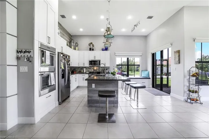 Kitchen with white cabinetry, stainless steel appliances, a breakfast bar area, a center island with sink, and a high ceiling