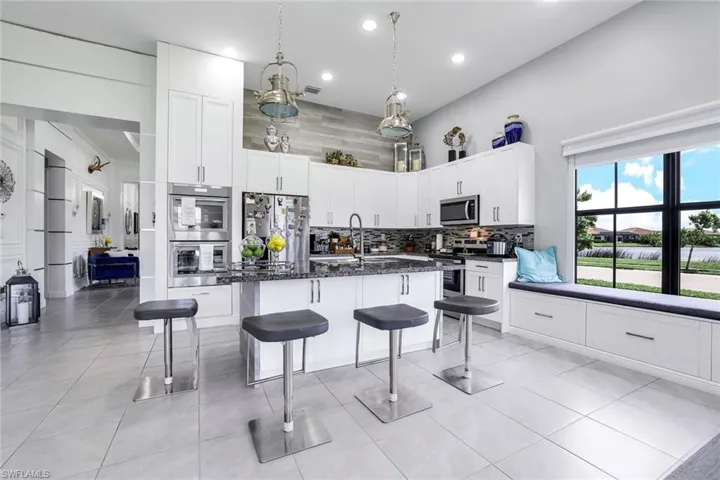 Kitchen with white cabinets, pendant lighting, a kitchen bar, appliances with stainless steel finishes, and a center island with sink