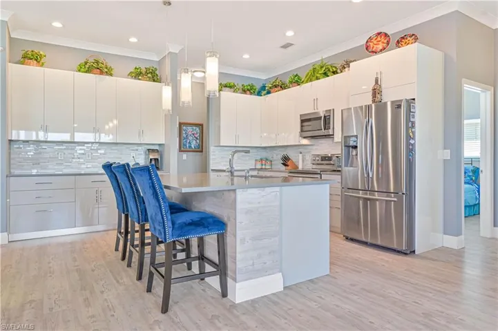 Kitchen with crown molding, a kitchen bar, a sink, appliances with stainless steel finishes, and hanging light fixtures