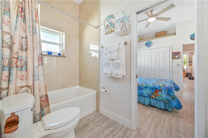 Full bathroom featuring toilet, shower / bath combination with curtain, a ceiling fan, baseboards, and wood finished floors