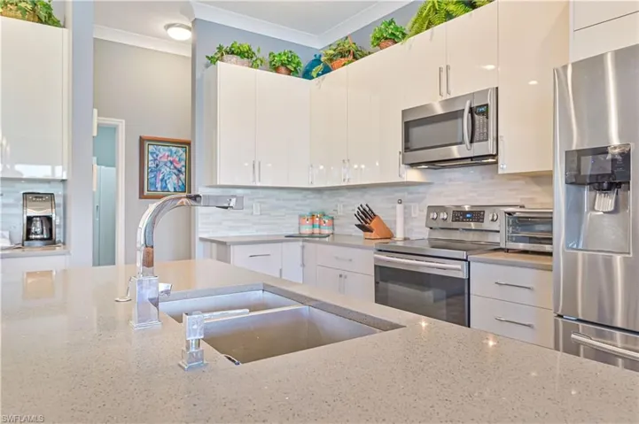 Kitchen featuring crown molding, a toaster, light stone countertops, a sink, and appliances with stainless steel finishes