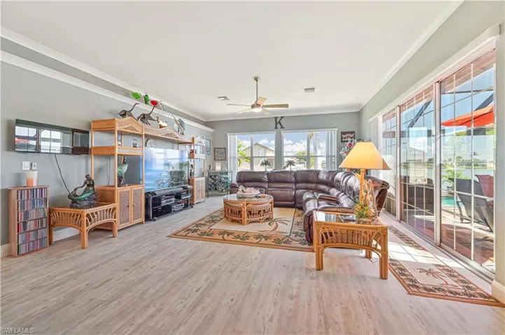 Living area with ceiling fan, baseboards, wood finished floors, visible vents, and ornamental molding