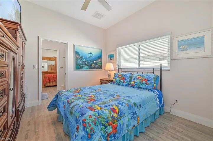 Bedroom with a ceiling fan, visible vents, wood finished floors, baseboards, and ensuite bathroom