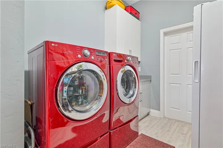Clothes washing area featuring separate washer and dryer, cabinet space, and wood finished floors
