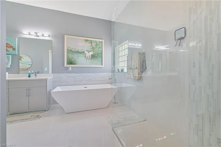 Bathroom featuring a freestanding bath, tile walls, walk in shower, vanity, and marble finish floor